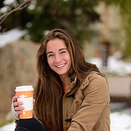 A student smiling at the camera holding coffee.
