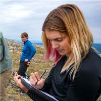 A student writes in a notebook while researching in the field.