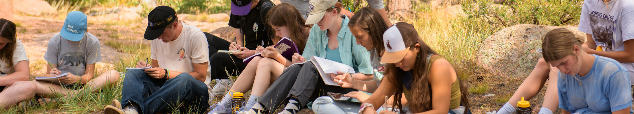 A group of students sit together reading outside near some large boulders.