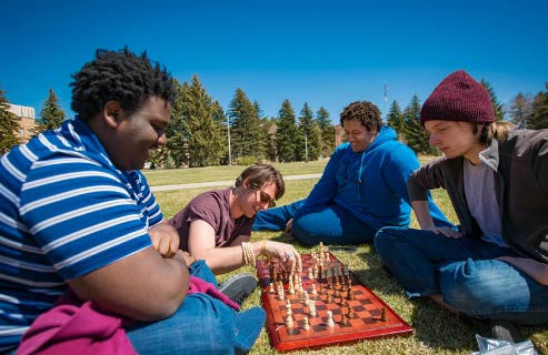 Three students sit together playin chess outside.