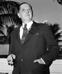 Arnold in a suit holding a cigar with palm tree in background