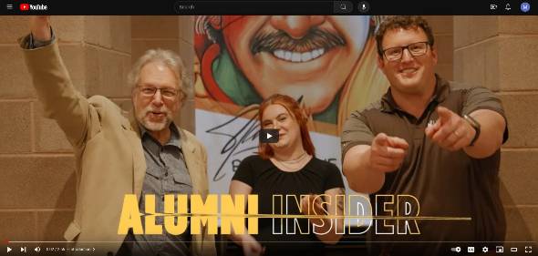 Alumni Insider image of Paul Flesher and Rhianan in front pf the stan lee banner