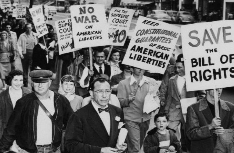 Well dressed actors standing in a picket line carrying picket signs with messages on American rights and liberties 