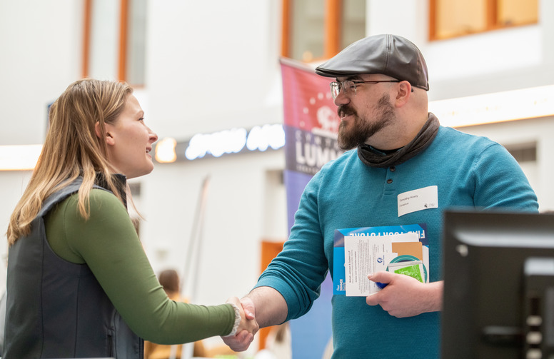 A student shaking hands with a business rep at a job fair.