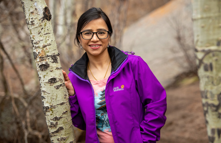 A student in a purple coat stands against an aspen tree.