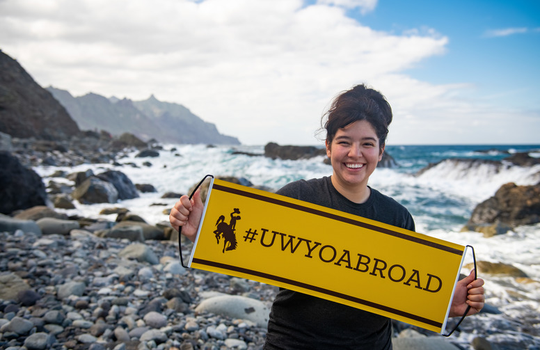 A UW student holding UWYO Abroad banner in front of the ocean.