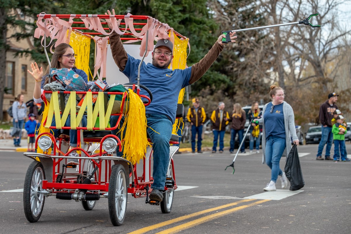 Volunteers ride a four-seater bicycle while picking up trash in the homecoming parade.