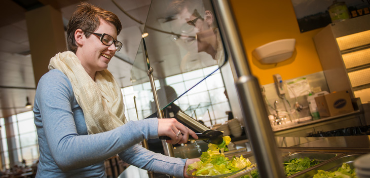Person putting lettuce on plate at the Washakie Dining Center salad bar
