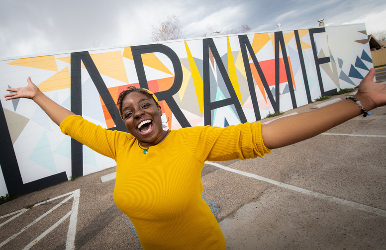 woman smiles in front of Laramie mural