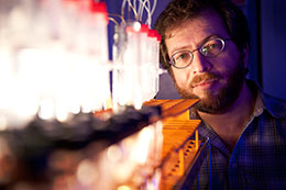 man standing behind lit-up scientific equipment