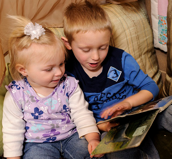 Children sharing a book. Older child reading to younger one