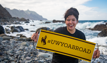 Student holding "#UWYOABROAD" banner in front of ocean