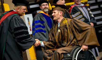 Student in wheelchair at graduation shaking hands with administrator on stage