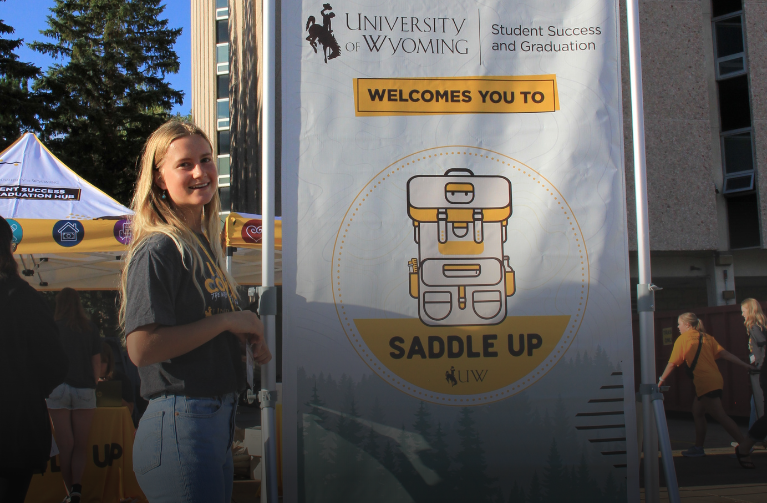 Student standing in front of Saddle Up banner