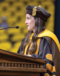 woman in cap and gown speaking at a podium